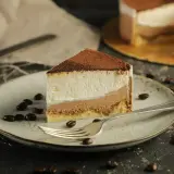 Pyszne ciasto tiramisu na biszkopcie, posypane kakao, na talerzu z kawowymi ziarnami i widelcem.