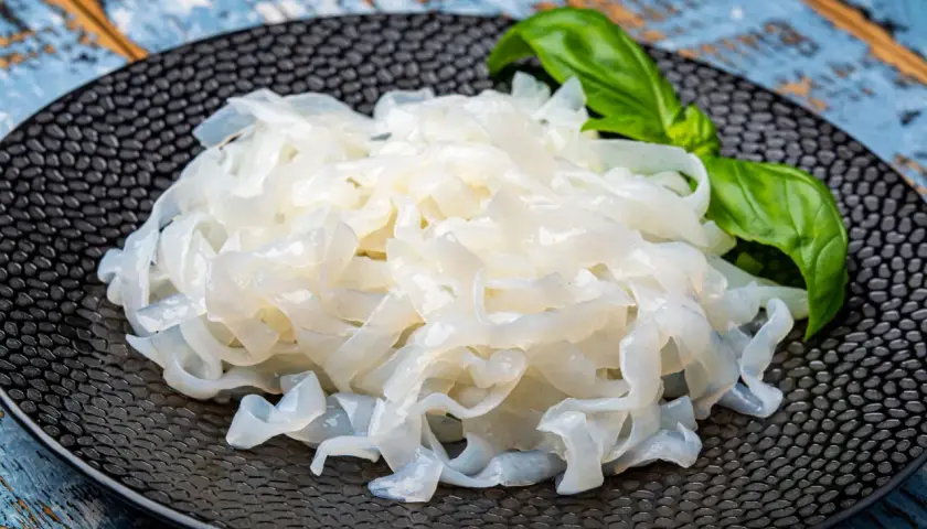 Makaron konjac na czarnym talerzu, z listkiem bazylii. To zdrowa alternatywa dla tradycyjnych klusek.