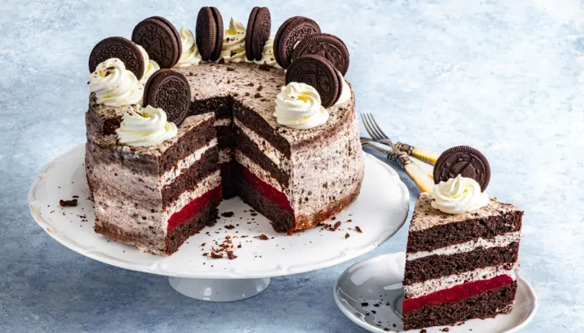 Przepis na tort oreo: czekoladowe blaty, krem z ciasteczkami, malinowa warstwa i dekoracja z bitej śmietany i ciastek oreo.